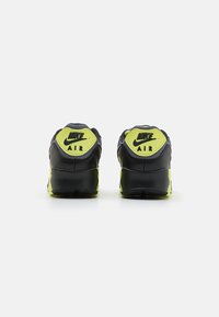 Black sneakers with bright yellow accents, featuring a textured surface, padded collar, and "Nike Air" branding at the heel.