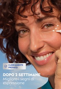 Primo piano di un volto sorridente con capelli ricci castani. Una mano applica una crema bianca sotto l'occhio. Il testo sottostante dice "Clinicamente Provato."