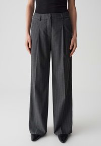 Pantalon gris à jambes larges en tissu texturé avec un motif à rayures, doté d'une taille ajustée et d'un devant plissé, associé à des chaussures noires.