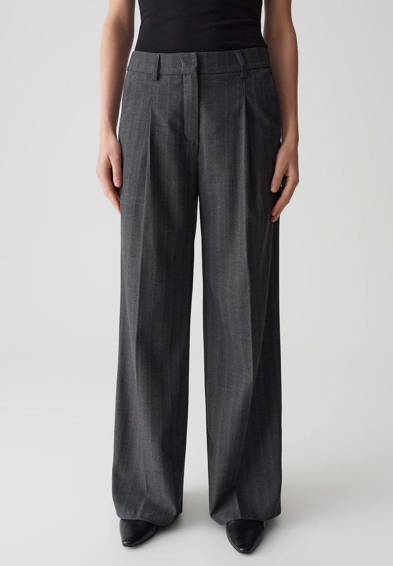 Pantalon gris à jambes larges en tissu texturé avec un motif à rayures, doté d'une taille ajustée et d'un devant plissé, associé à des chaussures noires.