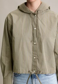 Gekürztes Shirt in olivgrün und cremefarbenem Karomuster, mit Kapuze, Frontknöpfen und Kordelzugsaum für eine verstellbare Passform.