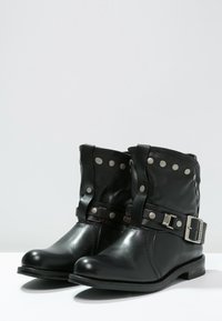Czarne skórzane botki na kostkę z szerokim mankietem, srebrnymi ćwiekami i ozdobnym paskiem z metalową klamrą. Płaska podeszwa z niewielkim obcasem.