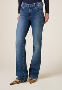 Jeans de campana en denim azul, con sutiles acentos de strass cerca de los bolsillos. Textura suave con diseño clásico de cinco bolsillos.