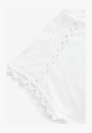 Camiseta blanca con bordes en forma de scallop y detalles decorativos recortados en las mangas, hecha de una tela suave y ligera.