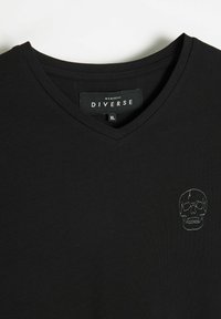 Czarna bawełniana koszulka typu v-neck z małym haftowanym wzorem czaszki po lewej stronie klatki piersiowej. Miękka tekstura, minimalistyczny design.