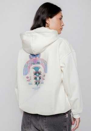 Sudadera crema con un gran gráfico en tonos pastel en la parte de atrás, que presenta patrones geométricos y diseños florales. Tejido suave, corte casual.