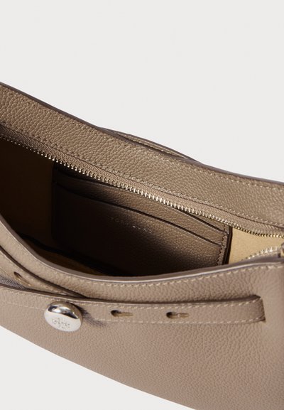 Ανοιχτή μπεζ δερμάτινη τσάντα με υφή, δείχνοντας τον φερμουάρ θάλαμο και το ραμμένο καπάκι με κλείσιμο από ασημένιο κουμπί.