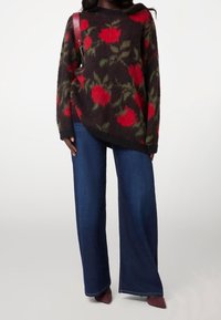 Maglione a fantasia floreale con rose rosse su sfondo scuro, caratterizzato da maniche oversize e orlo a coste, abbinato a jeans a gamba larga blu.