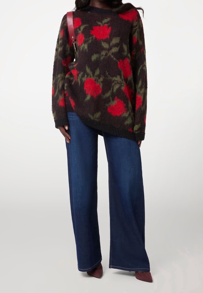 Maglione a fantasia floreale con rose rosse su sfondo scuro, caratterizzato da maniche oversize e orlo a coste, abbinato a jeans a gamba larga blu.