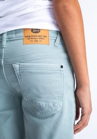 Pantaloni in denim azzurro chiaro con etichetta in pelle con il logo "Petrol", cuciture visibili e tasca posteriore con un dettaglio di bottone nero.