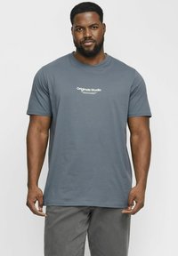 Grå kortærmet t-shirt lavet af blødt stof med runde halslinje og hvid "Originals Studio" tekst på fronten.