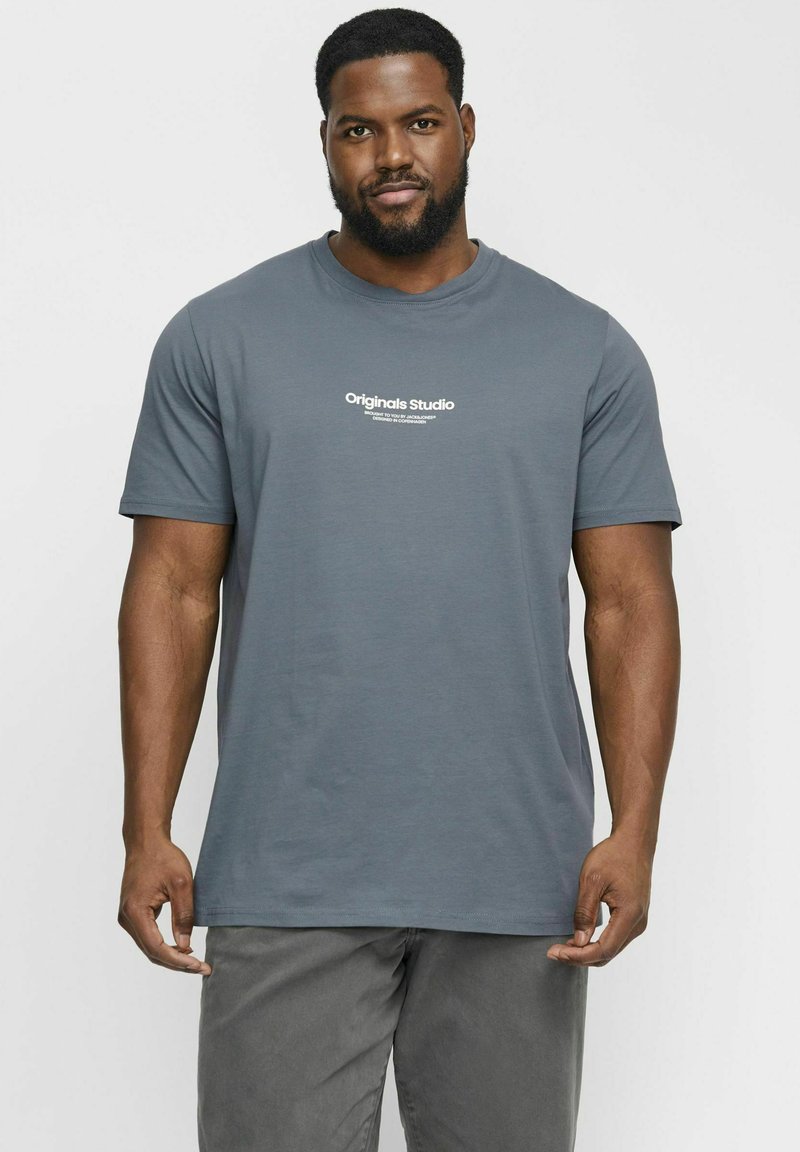 Grå kortærmet t-shirt lavet af blødt stof med runde halslinje og hvid "Originals Studio" tekst på fronten.