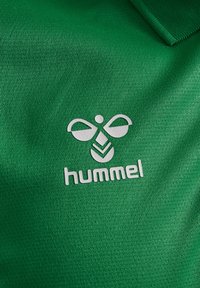 Grøn, tekstureret polo-shirt med et hvidt, præget logo, der har et stiliseret bi-design over teksten "hummel" i små bogstaver.