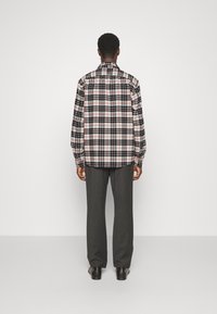 Camicia a scacchi con motivi neri, bianchi e rossi; maniche lunghe; vestibilità rilassata. Abbinata a pantaloni grigi e scarpe nere.