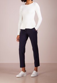 Top lungo a maniche lunghe a coste bianche con orlo a peplum, abbinato a pantaloni attillati blu navy e sneakers bianche. Design semplice e casual.