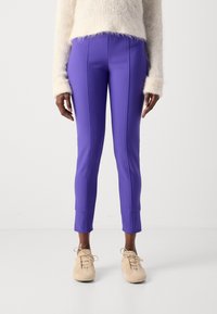 Strakke paarse broek met een gladde textuur en contrasterende naden, eindigend net boven de enkel, gecombineerd met lichtbeige schoenen.
