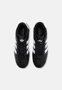 Svarta fotbollsskor i läder med vit tre-randig design, svarta skosnören och vadderad struktur på tåområdet. Logotyp på tungan.