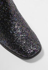 Gros plan d'une chaussure noire recouverte de paillettes multicolores avec un bout carré et une semelle noire lisse.