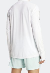 Biała sportowa koszulka z długim rękawem, z teksturowanym wzorem siateczki, o prostym kroju i z dodatkowym czarnym akcentem na lewym rękawie.