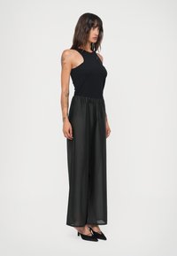 Black sleeveless top paired with sheer black wide-leg pants, featuring an elastic waistband and high-heeled black shoes.