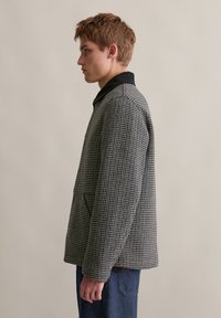 Grijs en zwart geblokte jas met een zwarte kraag, twee zijzakken en een relaxte fit. Geweven structuur zichtbaar.