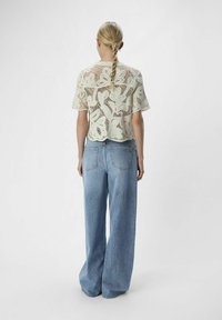Top de encaje con estampado floral, mangas cortas y dobladillo de picos; combinado con unos vaqueros sueltos de color azul claro; modelo visto desde la espalda.