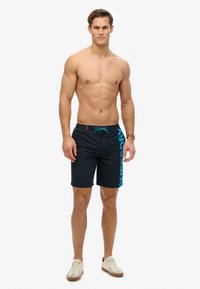 Pantaloni da nuoto navy con il testo turchese "SUPERDRY" di lato, fascia in vita con cordino e un tessuto leggero per il comfort.