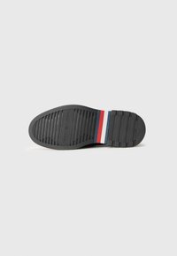 Semelle de chaussure en caoutchouc noir avec un motif de semelle horizontal. Présente une bande rouge, blanche et bleue près du talon. Texture lisse et forme arrondie.