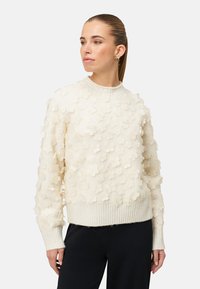 Kremfarvet sweater med teksturerede blomsterapplikationer, ribstrikkede ærmekanter og kant, samt en klassisk rund hals.