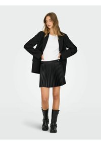 Must muströödiga mini-seelik sujuva vöökoha ja kullast nööbikaunistustega, koos valge ülaosaga ja suuremustasest bleiseriga. Mustad põlvini ulatuvad saapad.