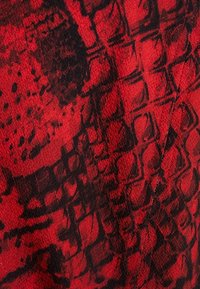 Röd tyg med en texturerad mönster som liknar ormskinn, med svarta inslag som är sammanflätade. Ytan verkar något grov.