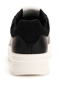 Zapatilla negra de cuero y ante con suela blanca, forma redondeada y área del talón acolchada, con un acabado suave y diseño minimalista.