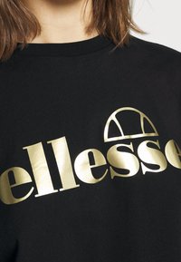 Sweatshirt noir avec un logo doré audacieux et un design graphique, doté d'un col rond classique et d'une texture de tissu douce.