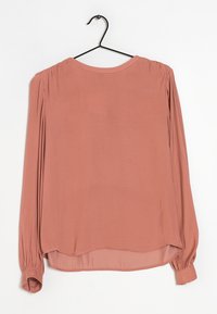 Blusa a maniche lunghe di colore rosa chiaro in un tessuto liscio. Presenta spalle arricciate e polsini elastici, con un orlo arrotondato sul retro.