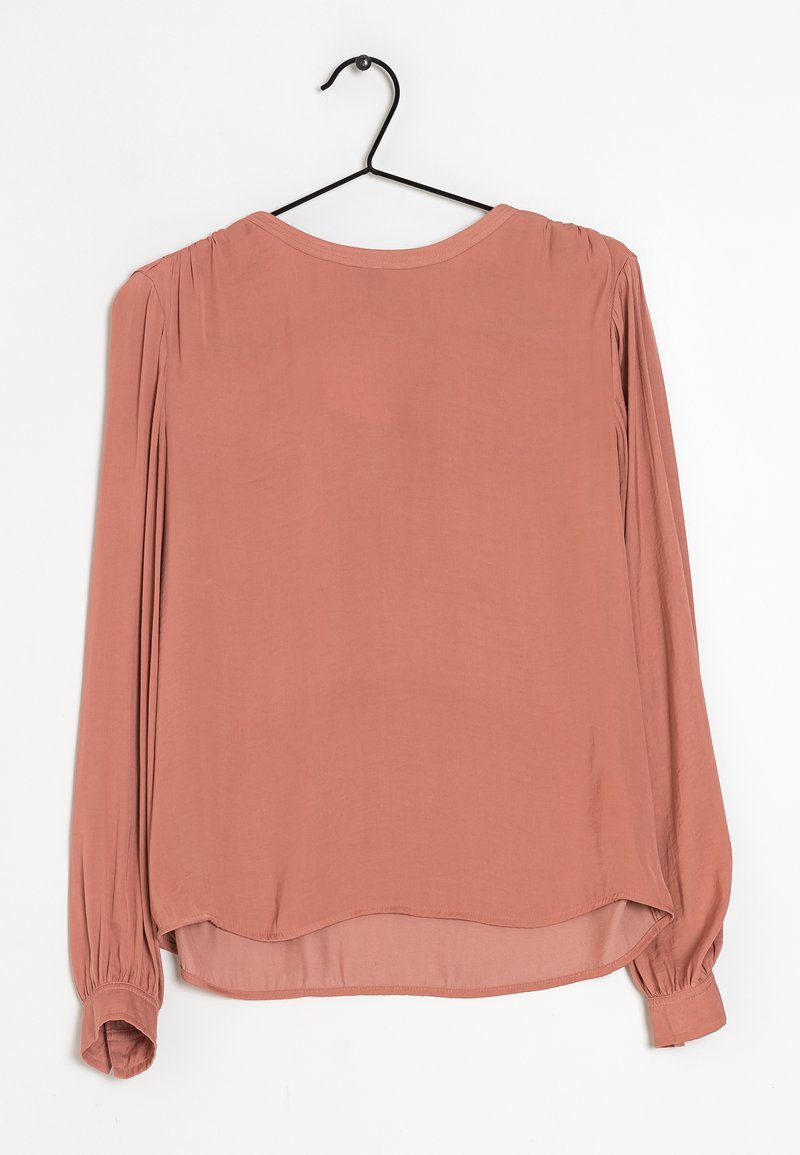 Blusa a maniche lunghe di colore rosa chiaro in un tessuto liscio. Presenta spalle arricciate e polsini elastici, con un orlo arrotondato sul retro.