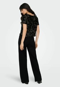 Haut noir à manches courtes recouvert de sequins, associé à un pantalon noir taille haute à jambes larges, avec une texture lisse.