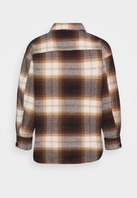 Bruin en witte geblokte wollen shirtjack met lange mouwen en knoopmanchetten, vanaf de achterkant weergegeven op een effen achtergrond.