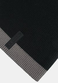 Sciarpa lavorata a maglia nera e grigia con una texture a coste e un bordo grigio distintivo. Un piccolo etichetta nera è attaccata vicino al bordo.