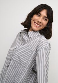 Chemise à boutons grise à rayures avec un col, dotée d'une poche poitrine et de rayures blanches verticales. Fabriquée en tissu léger et lisse.
