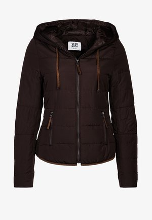 Kvinde iført sort dunjakke, sort-hvidstribet skjorte, lyseblå jeans, sorte ankelstøvler og bærende en brun skuldertaske.