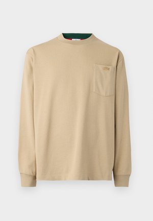 Beige skjorte med lange ermer og rund hals, med en brystlomme og logo-detalj. Mykt stoff med en jevn tekstur, enkel design.