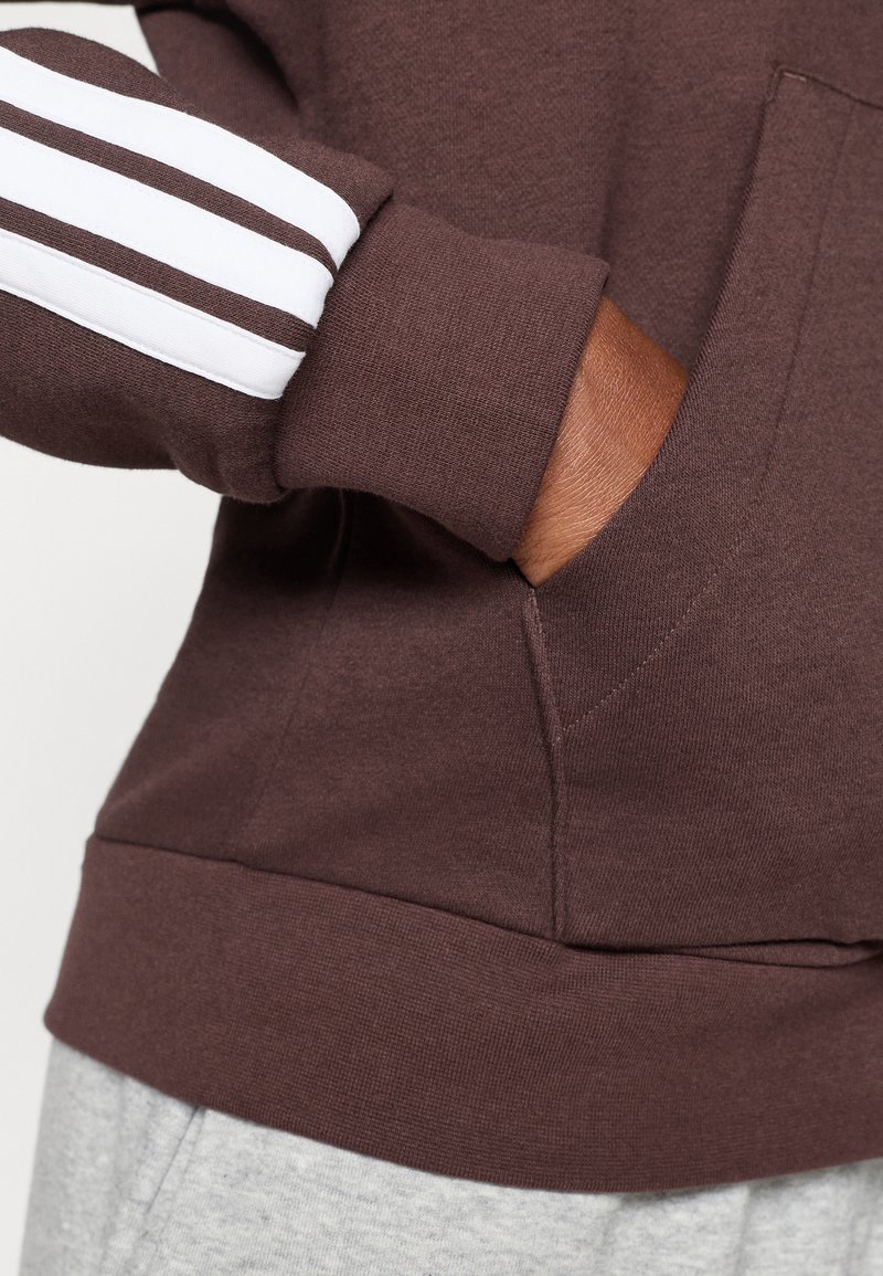 Bruine sweatshirt met witte gestreepte accenten op de mouwen, voorzien van een voorzak en geribbelde manchetten. Zachte stof met een ontspannen pasvorm.