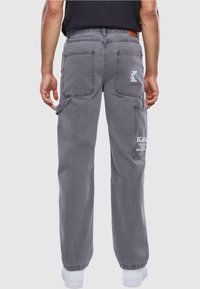 Pantalones cargo grises de algodón, con múltiples bolsillos, un ajuste relajado y un logo en el muslo derecho. Puños elásticos en los tobillos.