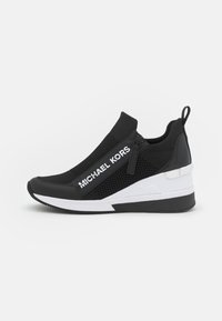 Musta lenkkari, jossa on verkko- ja synteettinen päällinen, jossa on wedgesohva, valkoiset yksityiskohdat, vetoketjutila ja "MICHAEL KORS" -brändäys.