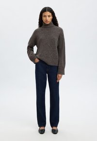 Pilkas golfas megztinis laisvo kirpimo su ribinėmis rankogaliais, derinamas su tamsiai mėlynais tiesaus kirpimo džinsais ir juodais butais su plokščiu padu.