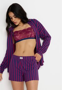 Conjunto de roupas de lazer listradas, com uma camisa de botão de mangas longas em rosa profundo e azul marinho, combinada com calções a condizer e um bralette de renda.