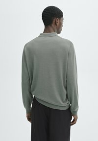 Long-sleeve polo in soft, muted green fabric with a smooth texture. Features a collar and relaxed fit, paired with dark pants.