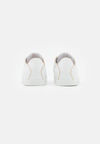 Sneakers bianchi in pelle con cuciture dorate sul tallone e sui lati, suola piatta e design a punta rotonda. Stile semplice e minimalista.