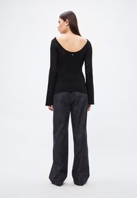 Fekete, hosszú ujjú felső mély kivágással a hátulján, vízszintes csíkos mintával. Magas derekú, széles szárú sötét farmernadrággal párosítva.