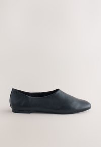 Chaussure plate en cuir noir avec bout arrondi, talon bas et modèle slip-on sur un fond clair uni.